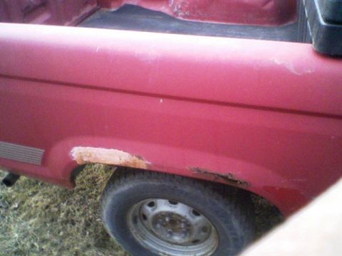 1992 Ford Ranger - Close-up of a red pickup truck's rear fender shows significant rust damage around the wheel well.