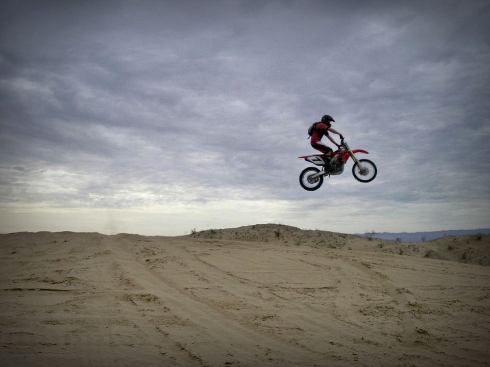 Red dirt bike airborne over sand dunes