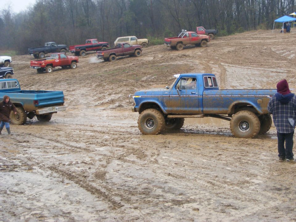 Muddy 1979 Ford F-250 pickup truck with large tires, parked on a dirt track with other trucks in the background