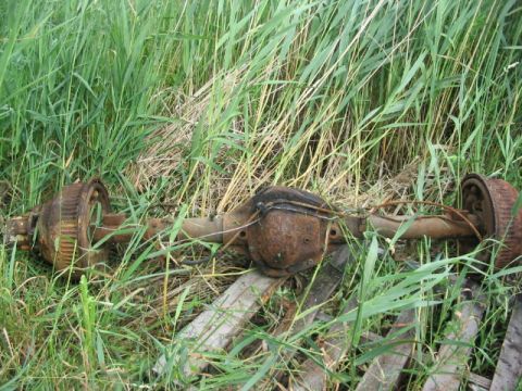 1986 Ford Bronco - A rusty rear axle assembly with brake drums is visible in tall grass.