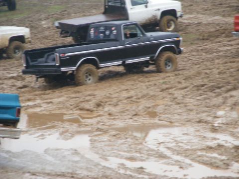 1979 Ford F-250 - A black pickup truck navigates a muddy terrain with other vehicles visible in the background.