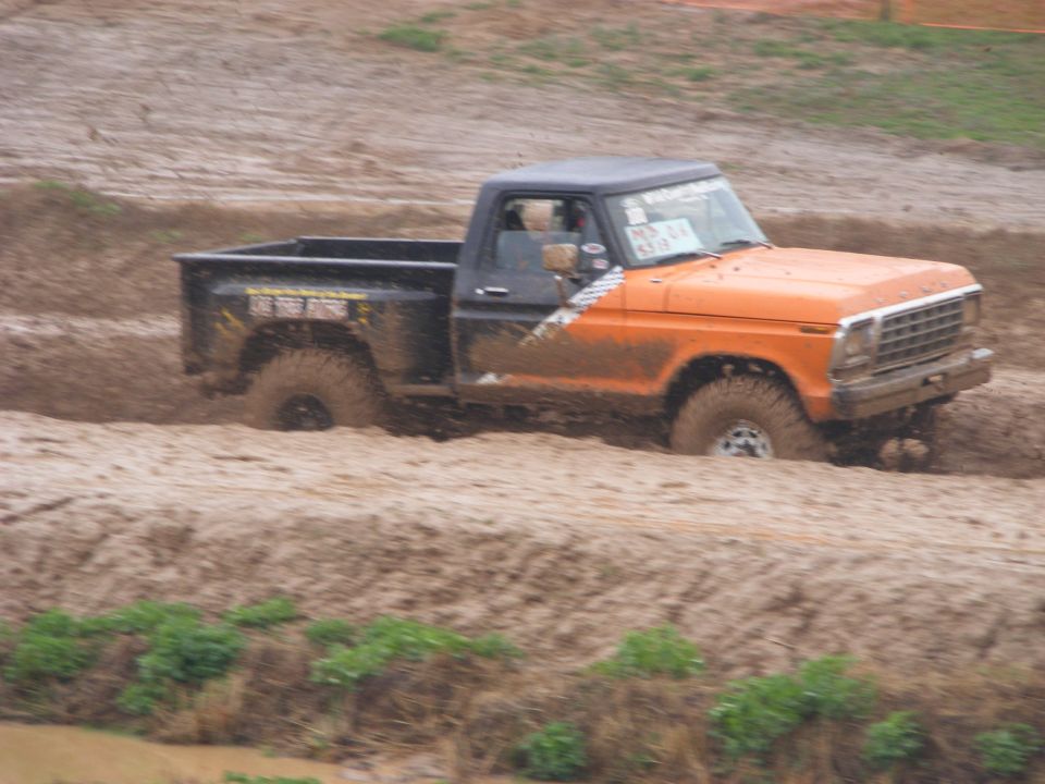 Orange and black Ford F-Series pickup truck driving through mud.
