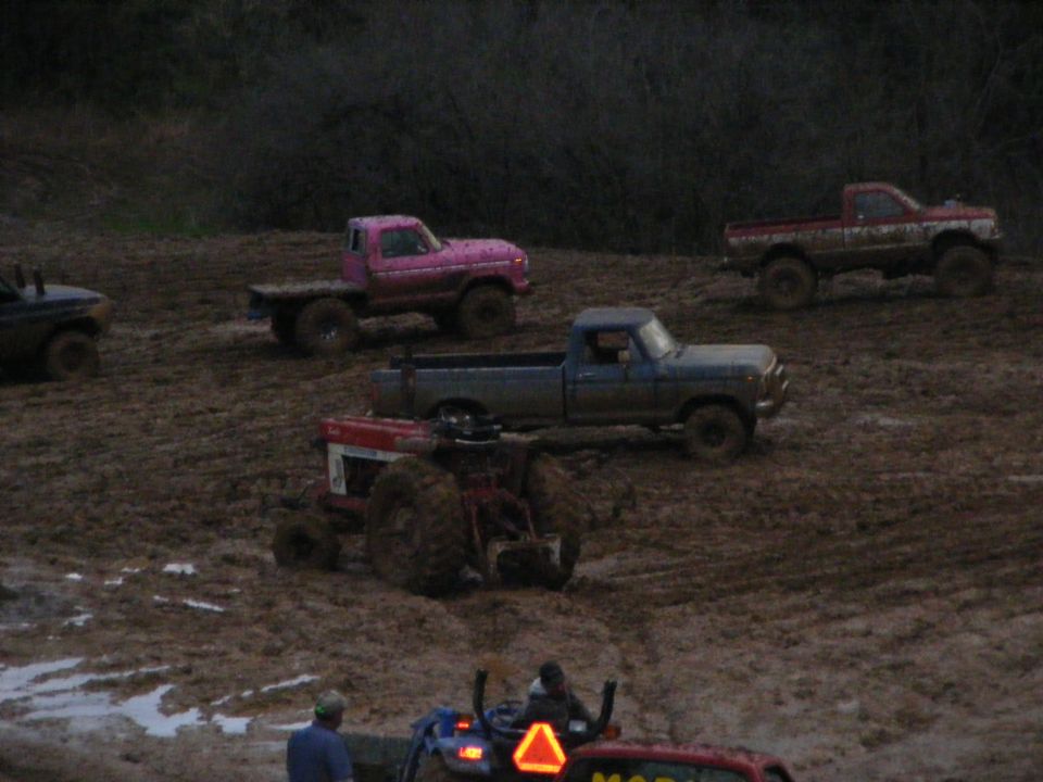 Muddy trucks and a tractor in a field.