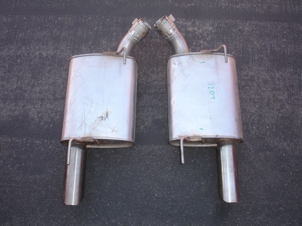Two stainless steel exhaust mufflers with chrome tips on a dark surface.