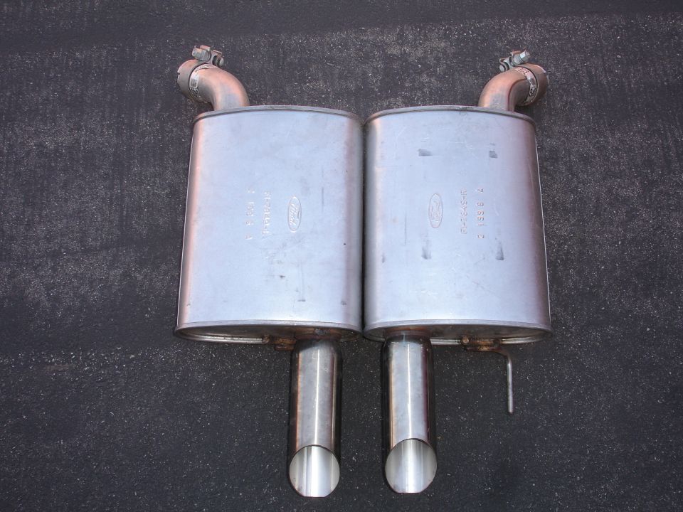 Two silver Ford mufflers with exhaust pipes on a dark surface.