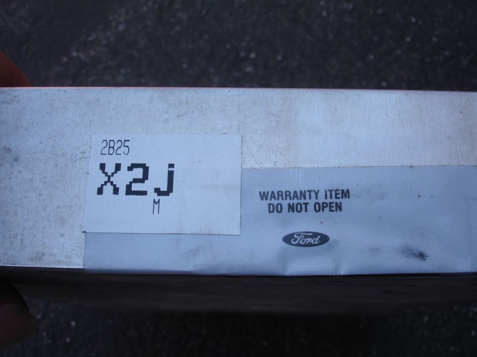 Silver box with labels showing '2B25 X2J M' and 'WARRANTY ITEM DO NOT OPEN' with a Ford logo
