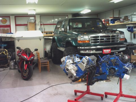 1996 Ford Bronco - A green Ford Bronco with a lifted suspension sits in a garage next to a motorcycle and two engines on stands.