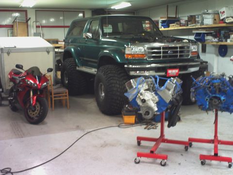 1996 Ford Bronco - A modified green Ford Bronco sits in a garage with a motorcycle and engine parts nearby.