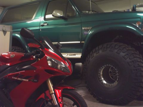 1996 Ford Bronco - A green 1996 Ford Bronco is parked next to a red motorcycle, both indoors.