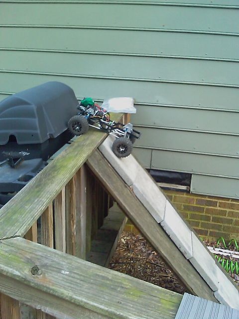 1996 Ford Bronco - A remote control rock crawler is positioned on a wooden ramp, with a grill visible to the left.