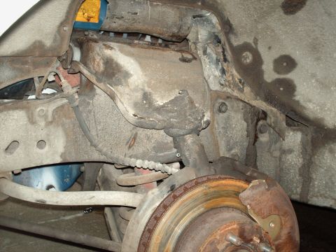 1973 Ford Ranchero - Grimy underside view of a front suspension corner with the wheel removed, showing the upper control arm, ball joint, coiled brake hose and…