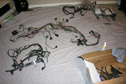 1984 Ford Bronco - A large automotive wiring harness is spread out on a grey blanket, with some components and a cardboard box in the foreground.