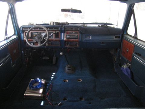 1984 Ford Bronco - The interior of a classic Ford Bronco shows a blue dashboard with wood grain accents, a steering wheel, and a manual transmission shifter.…