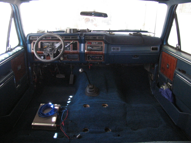 Interior of a classic Ford Bronco showing dashboard, steering wheel, shifter, and amplifier on the floor.