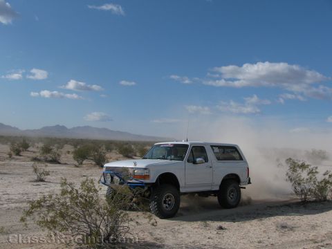 1990 Ford Bronco - Photo of a white Ford Bronco kicking up dust while off-roading in the desert, not a technical document.