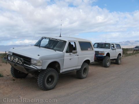 1990 Ford Bronco - Photo of two lifted Ford off-road trucks parked on a dirt road, not a technical document.