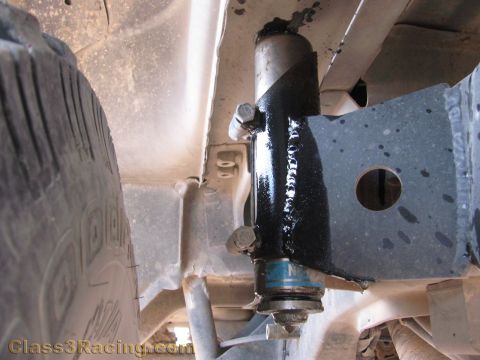 1990 Ford Bronco - Close-up of a black shock absorber bolted to a vehicle frame bracket beside a mud-terrain tire underneath the truck.