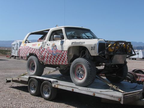 1990 Ford Bronco - white Bronco race truck numbered 317 with Big Boy and BFGoodrich graphics sits strapped on a tandem-axle flatbed trailer.
