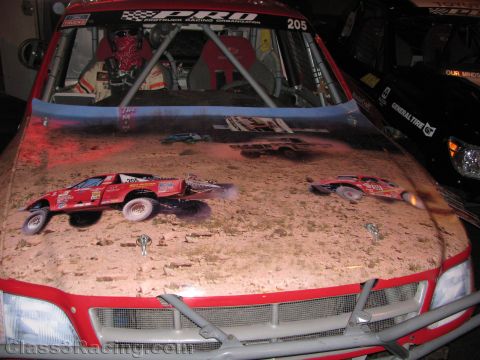 1990 Ford Bronco - red Pro Truck race truck displays an airbrushed hood mural of off-road trucks racing through desert terrain.