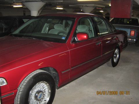 1997 Ford Crown Victoria - A red 1997 Ford Crown Victoria sedan is parked in a garage, with another vehicle visible behind it.