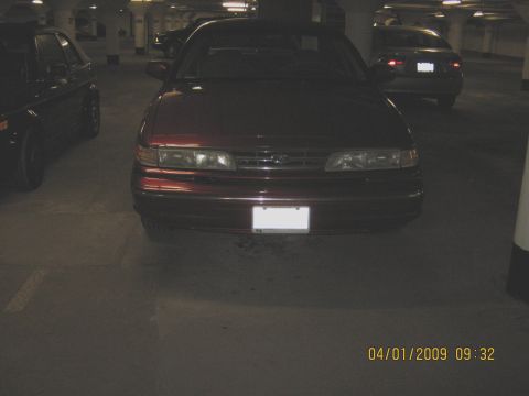 1997 Ford Crown Victoria - A red sedan is parked in a dimly lit garage, with other vehicles visible in the background.