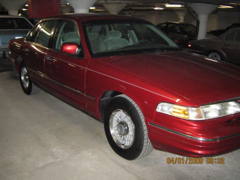 1997 Ford Crown Victoria - A red 1997 Ford Crown Victoria sedan is seen from the front-three-quarter angle in an indoor parking garage.