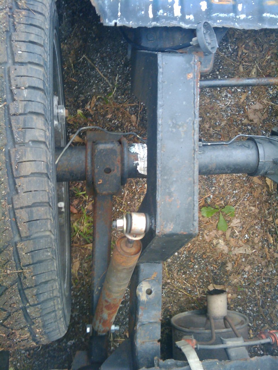 Close-up of a vehicle's rear axle, shock absorber, and tire. The frame is visible at the top