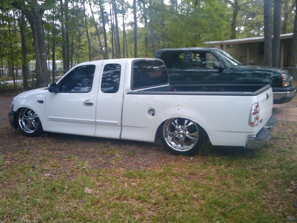 White 2000 Ford F-150 lowered with chrome wheels, parked next to a dark green pickup truck