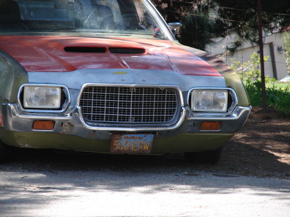 Front end of an early 1970s Ford in green and primer with scooped orange hood