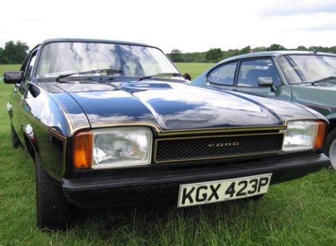 1973 Ford Ranchero - Black Ford Capri II coupe photographed from a low three-quarter front angle on a grass show field, showing gold pinstriping along the fende…