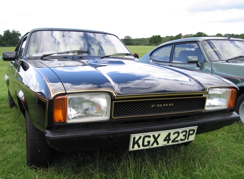 Black Ford Capri II coupe front three-quarter view on grass, gold pinstripe and UK plate KGX 423P