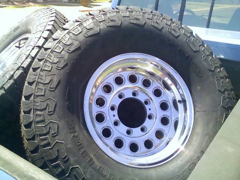 1996 Ford Bronco - Off-road tires and chrome 8-lug wheels are loaded into the bed of a truck.