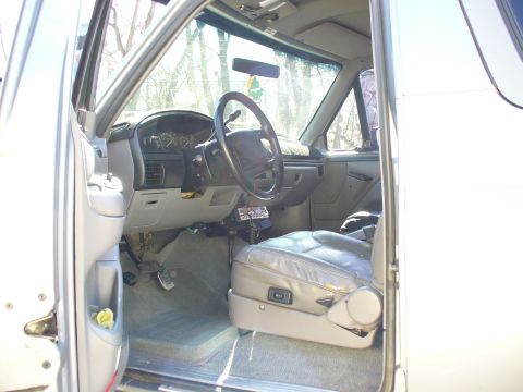 1994 Ford Bronco - The interior of a silver SUV shows gray leather seats and a dashboard with a steering wheel and CB radio.