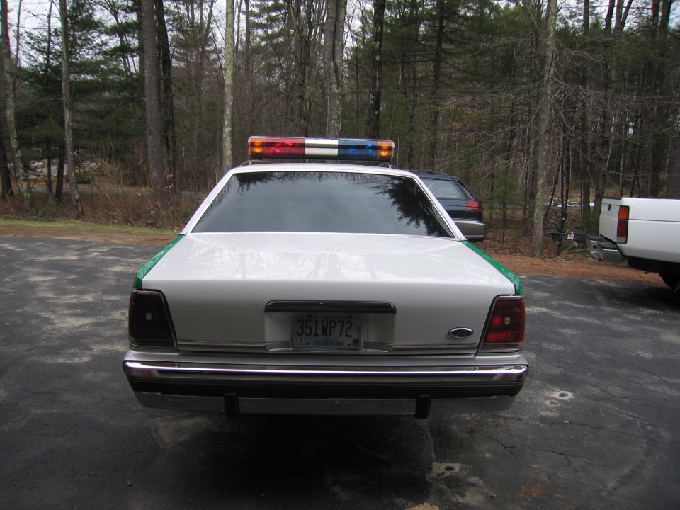 Rear of white-and-green Ford sedan with roof lightbar and 35LWP72 plate