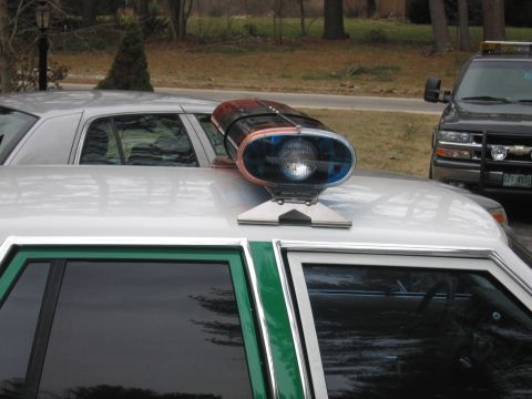 1991 Ford LTD Crown Victoria - Close-up of a rotating red-and-blue roof lightbar mounted on the roof of a green-and-white sedan, with a dark SUV in the background.