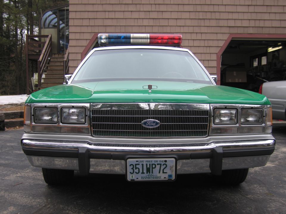 Close front view of green-hood Ford police sedan with light bar