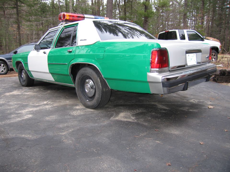 Green and white Ford police sedan, rear three-quarter view in driveway