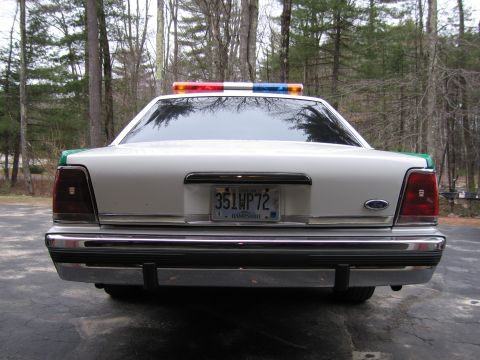 1991 Ford LTD Crown Victoria - Rear view of a white-trunked Ford sedan with roof light bar, chrome bumper, Ford emblem, and New Hampshire 351WP72 plate.