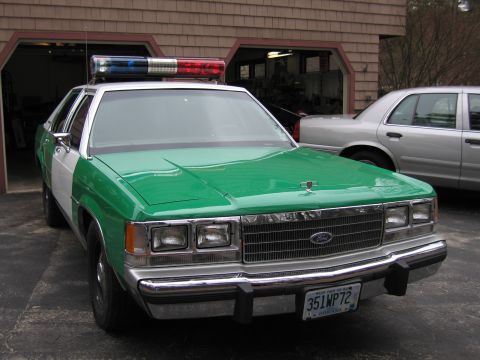 1991 Ford LTD Crown Victoria - Front view of a green-and-white Ford police sedan with roof light bar and a New Hampshire license plate reading 351WP72.