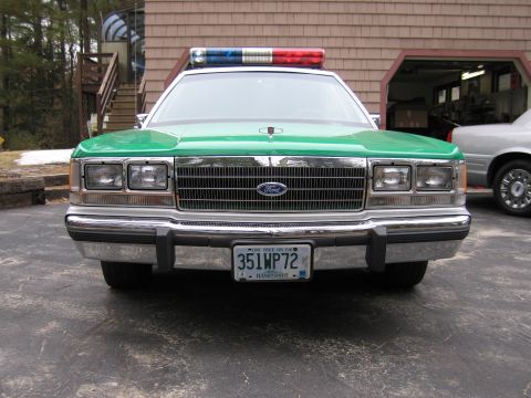 1991 Ford LTD Crown Victoria - Front view of a green-and-white Ford police sedan with roof light bar and New Hampshire plate 351WP72 in a driveway.