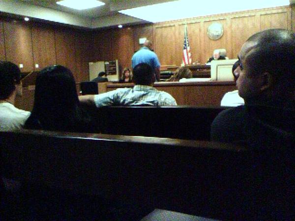 Courtroom scene from gallery with spectators, a judge at the bench, and an American flag