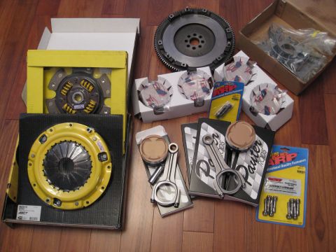 1994 Ford Probe - Engine rebuild parts laid out on a wooden floor, including a clutch, flywheel, pistons, and connecting rods.