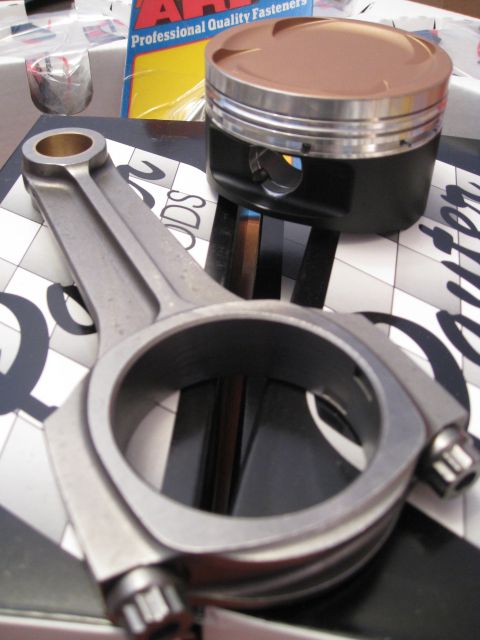 1994 Ford Probe - Engine components, including a connecting rod and piston, are displayed on a patterned surface with packaging in the background.