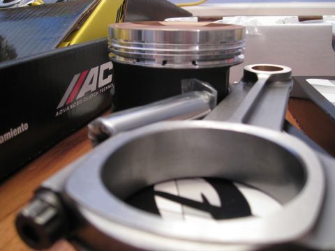 1994 Ford Probe - Engine components, including a piston and connecting rod, are laid out on a wooden surface next to a box from MAC Advanced Clutch Technolog…