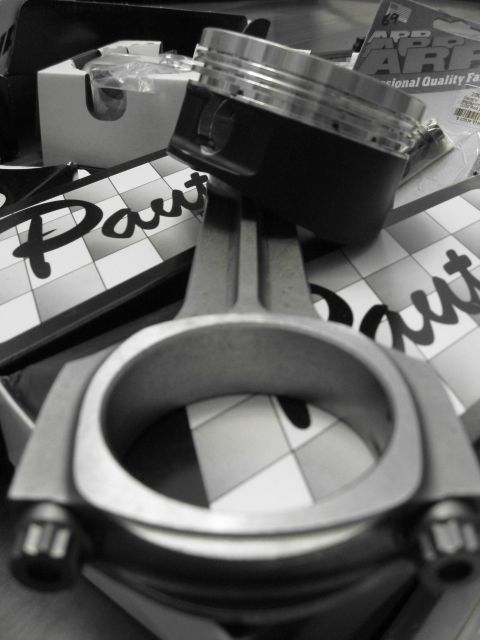 1994 Ford Probe - Close-up of engine components, a piston and connecting rod, resting on a surface with a checkered pattern and partial text.