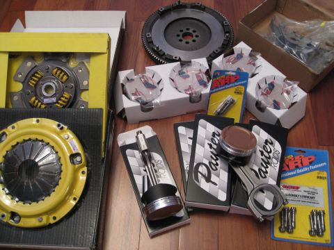 1994 Ford Probe - Various engine components are laid out on a wooden floor, including a clutch kit and pistons.