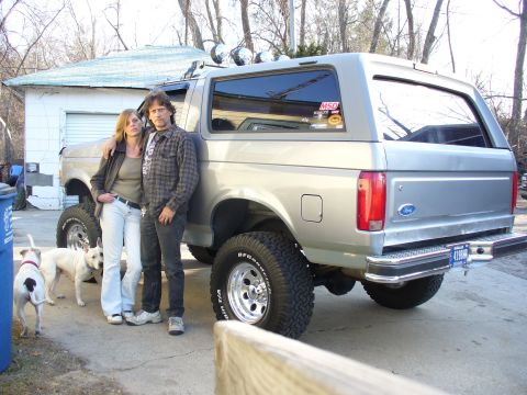 1994 Ford Bronco - A silver 1994 Ford Bronco is parked outside a garage with two people and two dogs standing nearby.