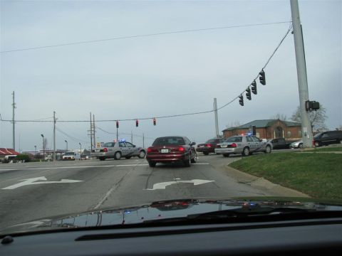 2003 Mercury Marauder - Multiple police cars and civilian vehicles are stopped at a traffic light intersection under an overcast sky.