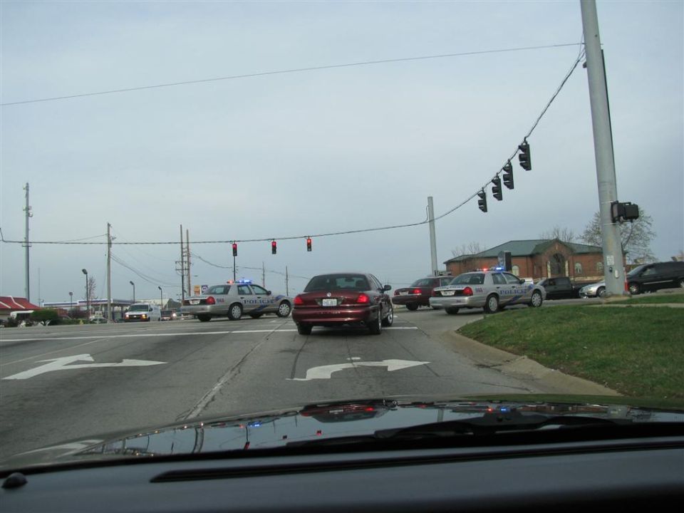 Red 2003 Mercury Marauder and police cars at intersection, overcast sky