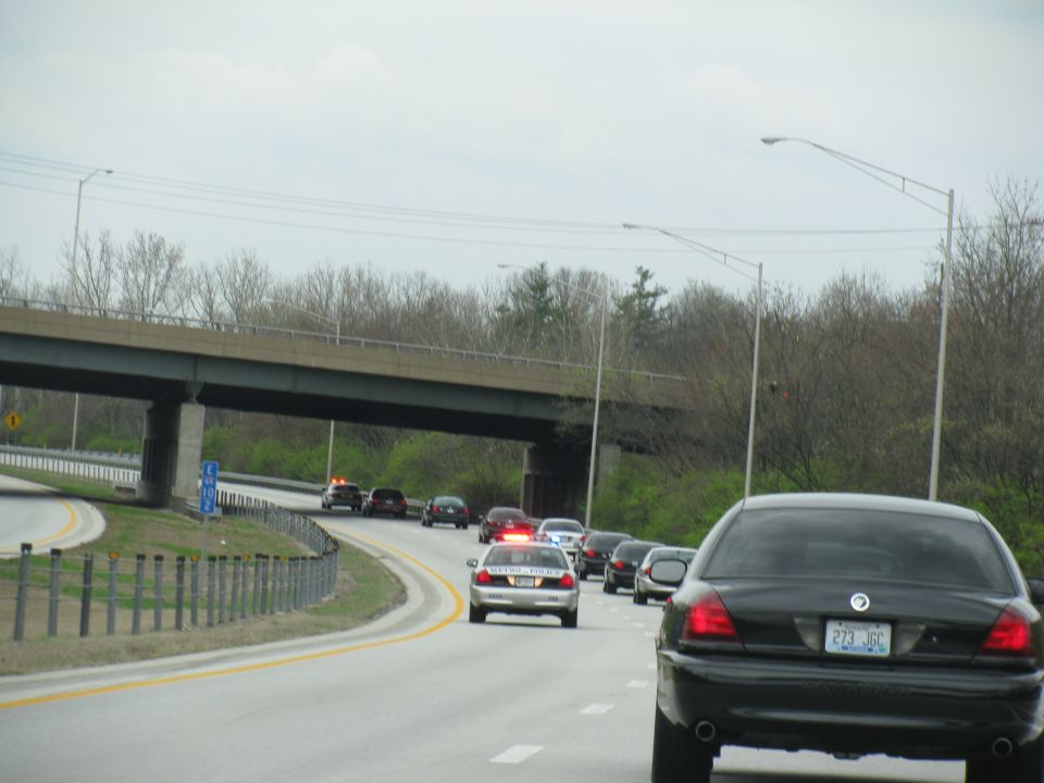 Driving on highway, several cars ahead, including police cars with lights on. Black car in foreground